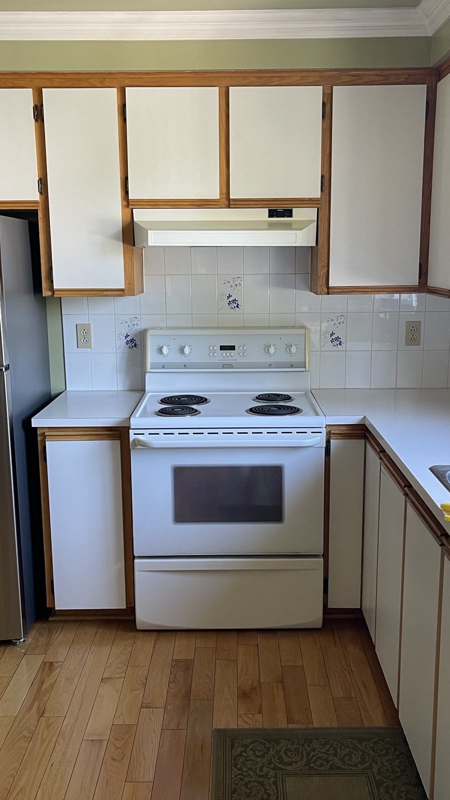 Avant — mur de cuisinière en mélamine encadrée de chêne, ancienne hotte blanche et dosseret de céramique à motifs
