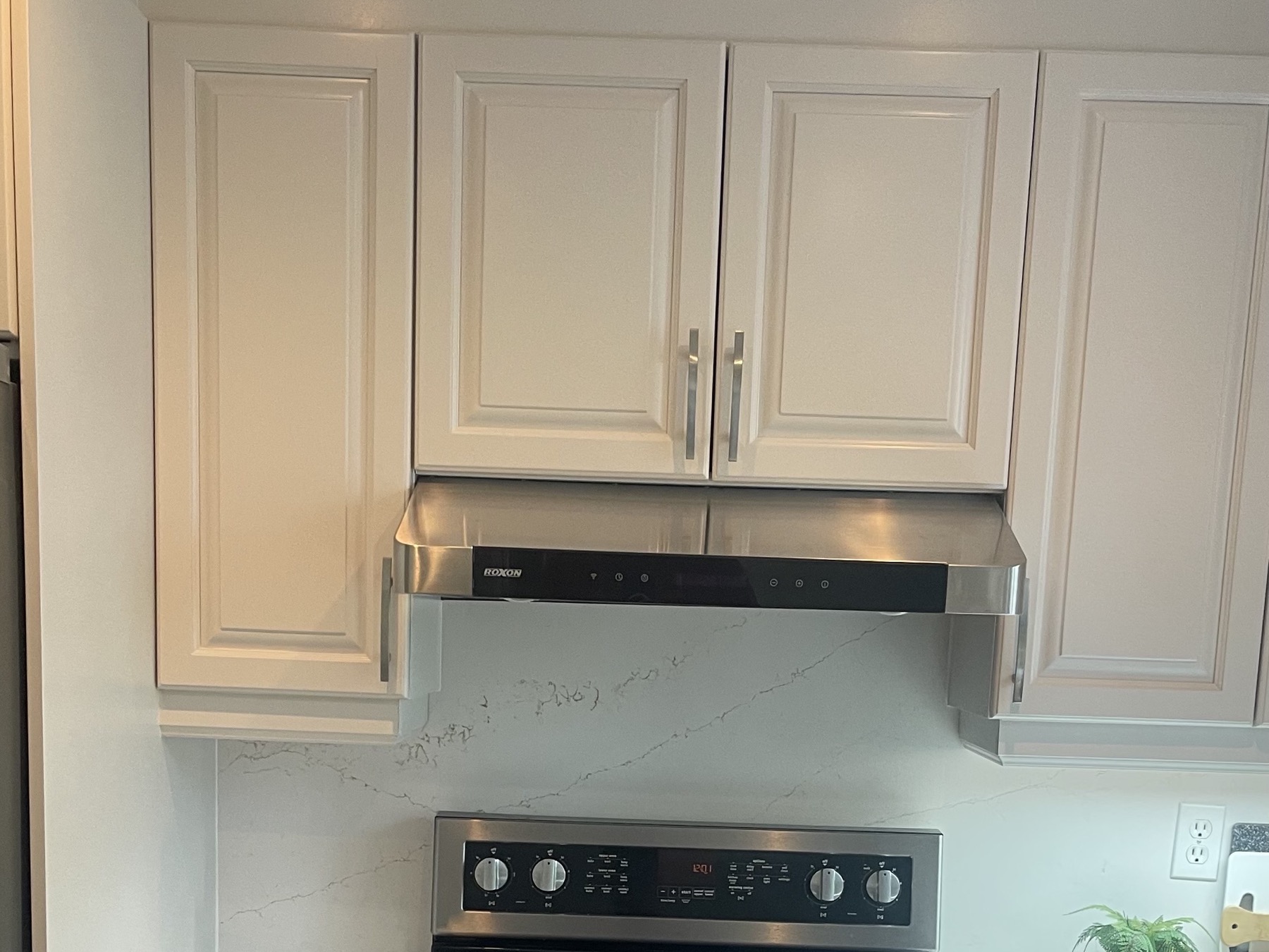 Kitchen after refacing — cream doors, veined quartz backsplash and stainless hood