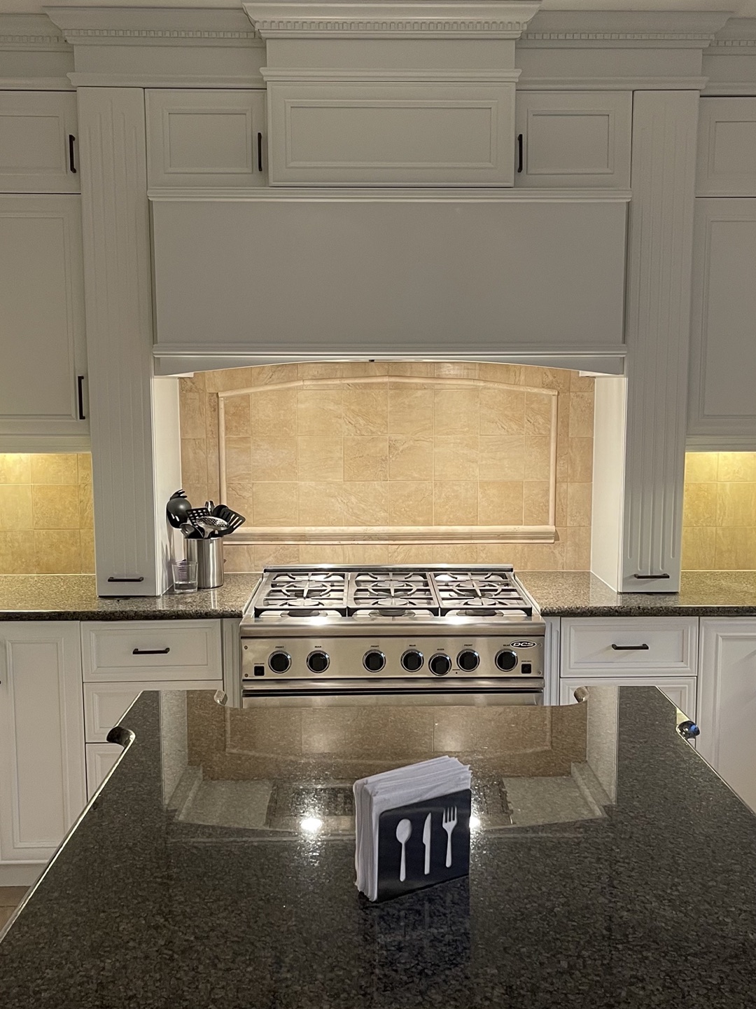 Mur de la cuisinière — cuisinière à gaz, dosseret de pierre beige cintré, comptoir de granit foncé