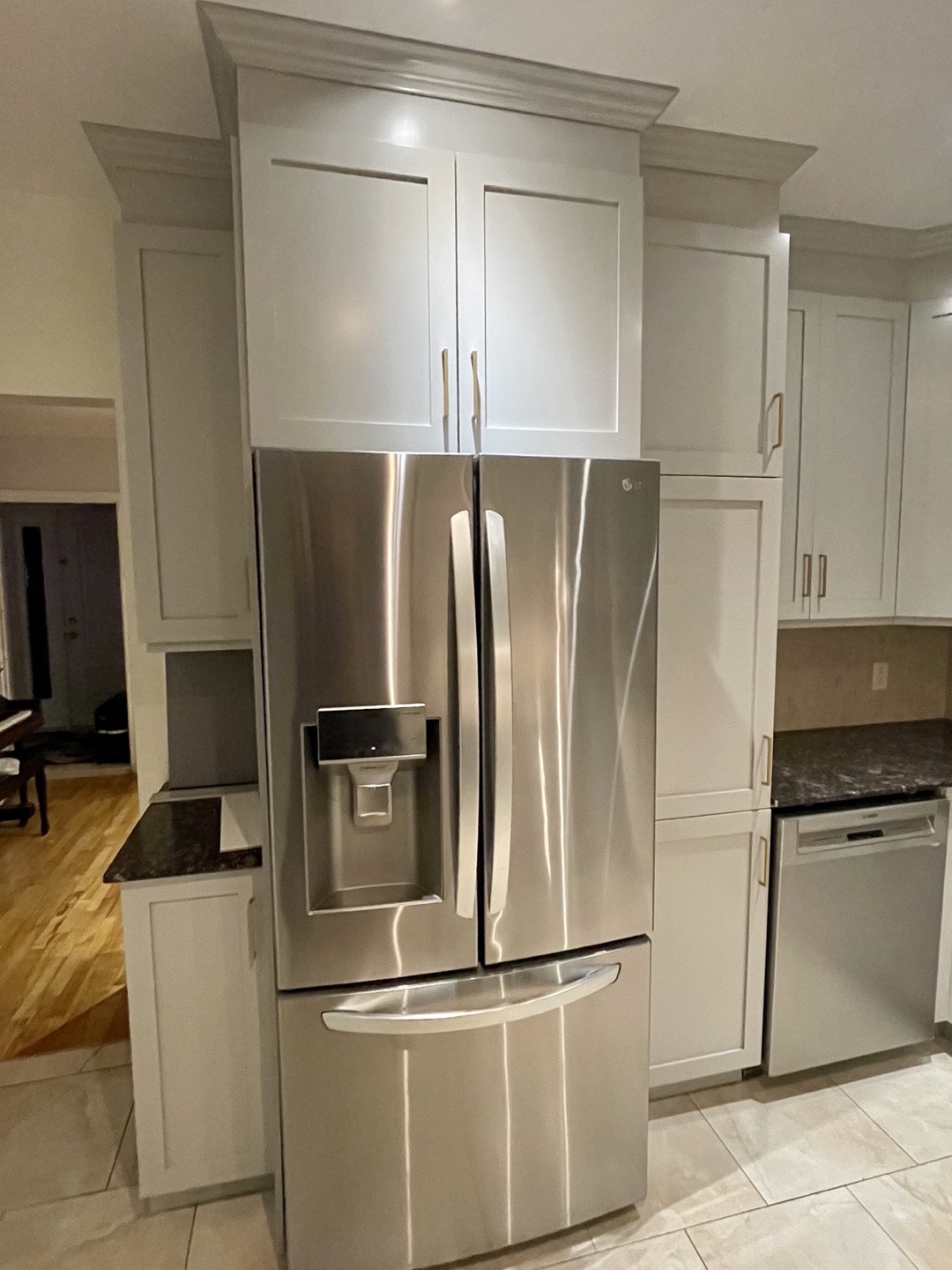Colonne de rangement et armoires refinies gris pale encadrant le refrigerateur en inox, moulure de couronnement et plancher de tuile.